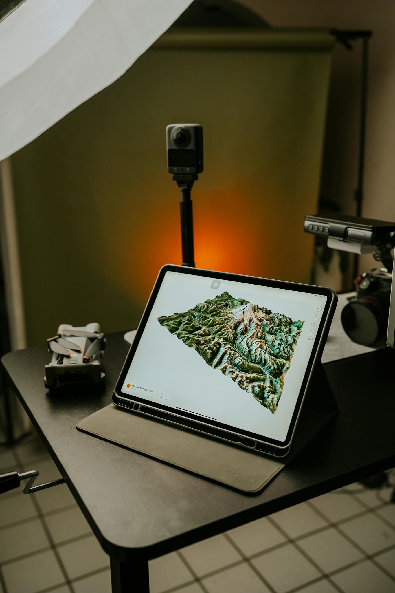High-tech setup featuring a tablet displaying 3D mapping, surrounded by drones and photography gear.